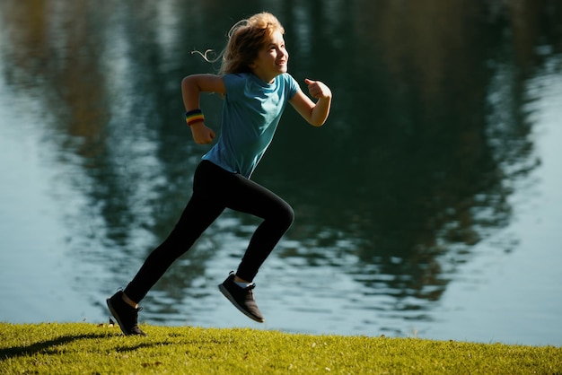 Kinder, die in der Nähe des Sees auf Gras im Park laufen oder joggen. Jungenläufer, die im Park im Freien joggen