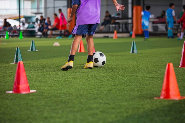 Kinder, die Kontrollfußball-Taktikkegel auf Rasenplatz mit für Trainingshintergrund spielen, der Kinder im Fußball ausbildet