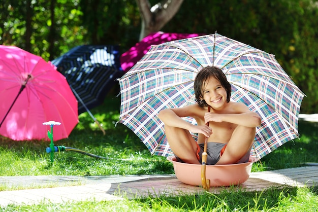 Kinder, die mit dem Berieselungsanlagenwasser hält Regenschirm auf Sommerhinterhof spielen