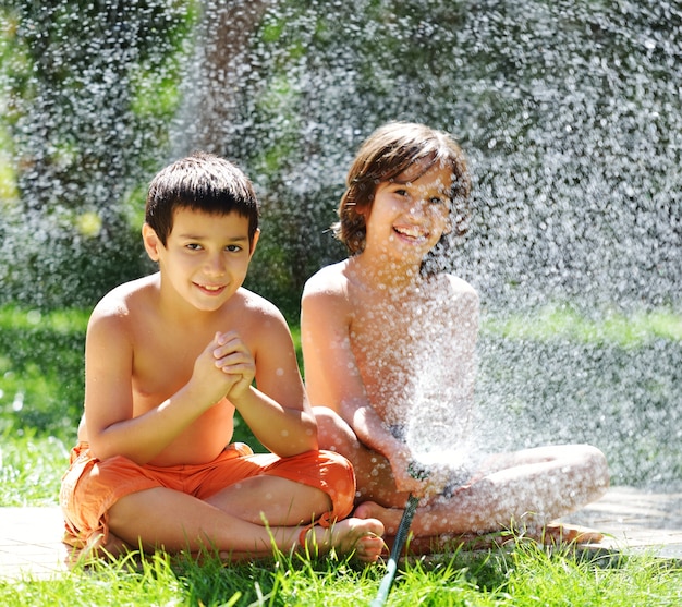 Kinder, die mit Wassersprenger auf Sommergrashof spielen und spritzen