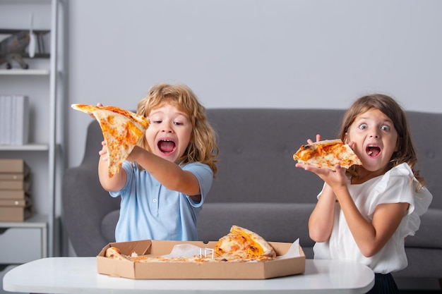 Kinder, die Pizza essen Aufgeregte Kinder, die Pizza essen Zwei kleine Kinder beißen Pizza drinnen