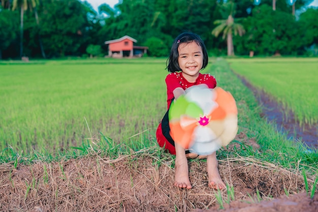 Kinder, die Regenbogenwindrad oder -windmühle auf Natur spielen Asiatische Kinder, die auf Grund von lächeln und sitzen