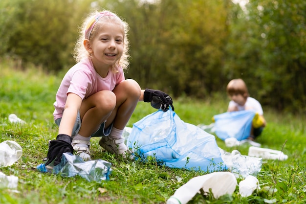 Kinder entfernen plastikmüll und stecken ihn in einen biologisch abbaubaren müllsack im freien. das konzept der ökologie, abfallverarbeitung und naturschutz. umweltschutz.