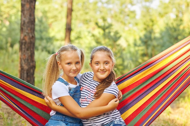 Kinder entspannen sich in der bunten Regenbogen-Hängematte. Heißer Tag, Gartenspaß im Freien. Mittagsschläfchen während der Sommerferien. Kinder entspannen sich