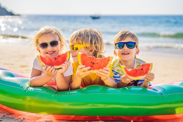 Kinder essen Wassermelone am Strand mit Sonnenbrille