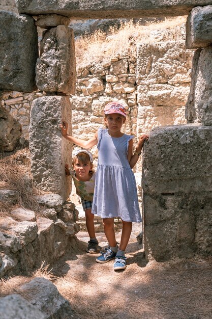 Kinder, Geschwister, Mädchen und Jungen reisen und erkunden die antiken Ausgrabungen der Ruinen der antiken lykischen Stadt Phaselis in der Türkei während der Sommerferien in der Natur in den Bergen im Freien