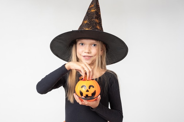 Kinder Halloween Ein wunderschönes süßes Mädchen in einem Hexenkostüm mit Hut holt Süßigkeiten aus einem Korb in Form von Jacks Laterne