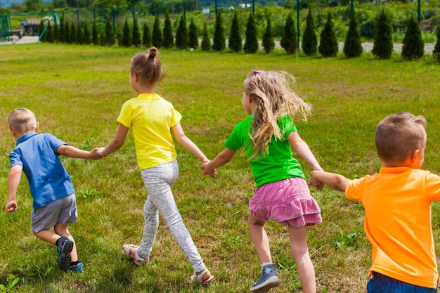 Kinder halten sich an den Händen und laufen. Sommerlager im Freien, Blick von hinten