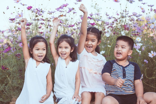 Kinder heben Hände an und spielen zusammen im Kosmosblumenfeld in der Sommerzeit