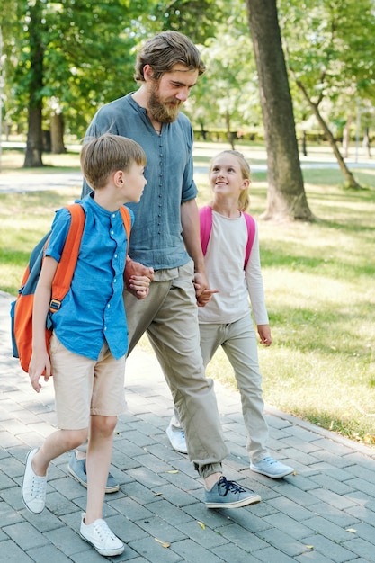 Kinder hören dem Vater zu, während sie zusammen zur Schule gehen