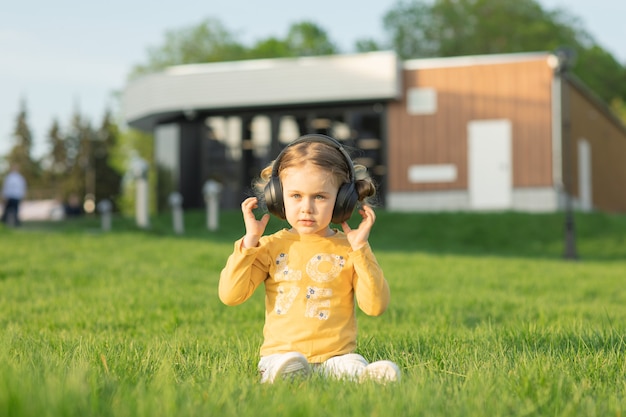 Kinder hören Musik in Kopfhörern genießen Lied im Radio sitzen auf der grünen Graswiese in der Parksommer-Playlist