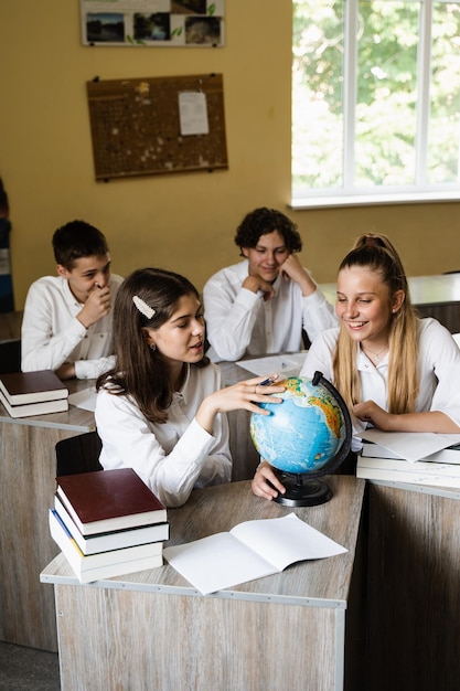 Kinder im Erdkundeunterricht schauen sich den Globus an und diskutieren über verschiedene Länder Bildungskonzept Schulkinder drehen den Globus und kommunizieren miteinander