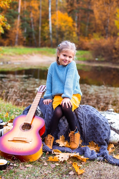 Kinder im Herbstwald auf einem Picknick Grillwürste und Gitarre spielen