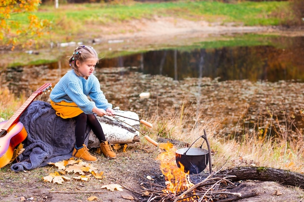 Kinder im Herbstwald auf einem Picknick Grillwürste und Gitarre spielen