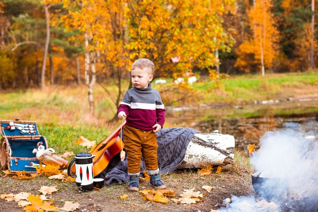 Kinder im Herbstwald auf einem Picknick Grillwürste und Gitarre spielen