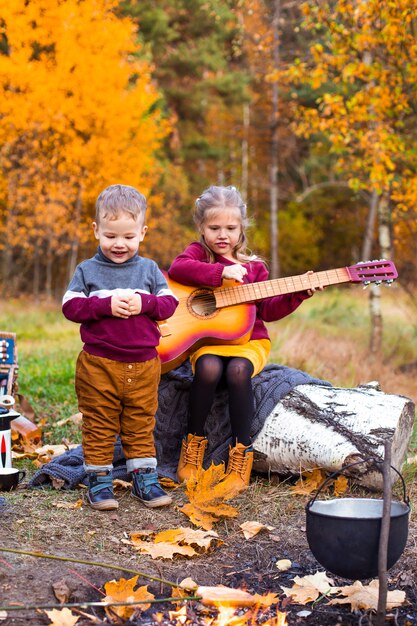 Kinder im Herbstwald auf einem Picknick Grillwürste und Gitarre spielen