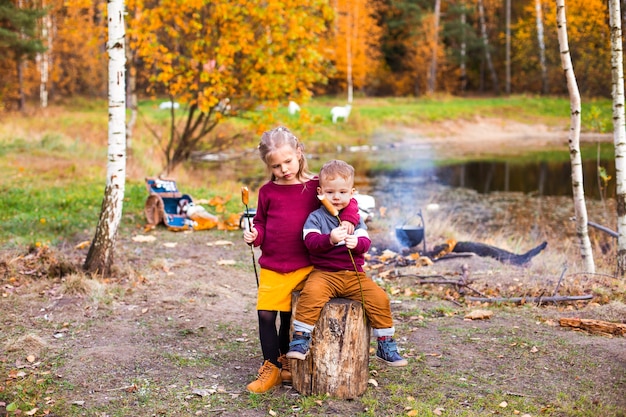 Kinder im Herbstwald auf einem Picknick Grillwürste und Gitarre spielen