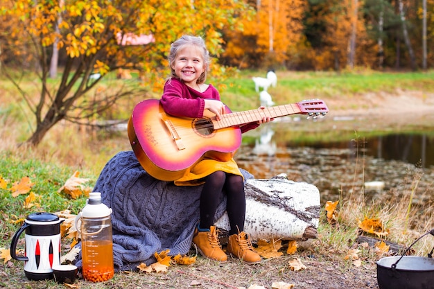 Kinder im Herbstwald spielen auf einem Picknick Gitarre