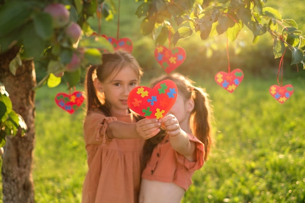 Kinder im Park bei Sonnenuntergang und zeigen am Autismus-Tag ein Herz aus farbigen Puzzleteilen