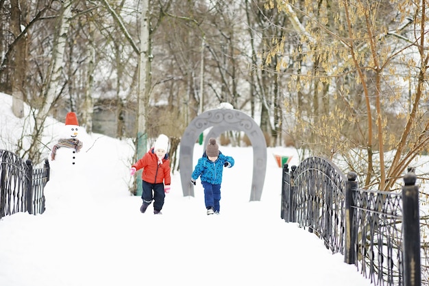 Kinder im Park im Winter. Kinder spielen mit Schnee auf dem Spielplatz. Sie formen Schneemänner und rutschen die Hügel hinab.