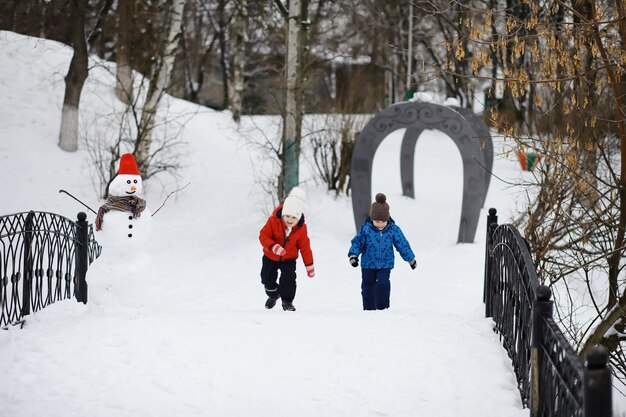 Kinder im Park im Winter. Kinder spielen mit Schnee auf dem Spielplatz. Sie formen Schneemänner und rutschen die Hügel hinab.