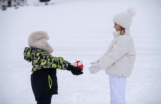 Kinder im Schnee Ein kleiner Junge in Winterkleidung gibt einem kleinen Mädchen ein Geschenk in Form eines Herzens