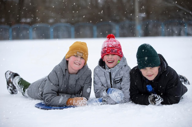 Foto kinder im winter drei kleine freunde liegen im schnee und schauen in die kamera