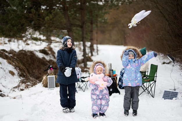 Kinder im Winterwald bei einem Picknick mit Stofftieren an den Händen