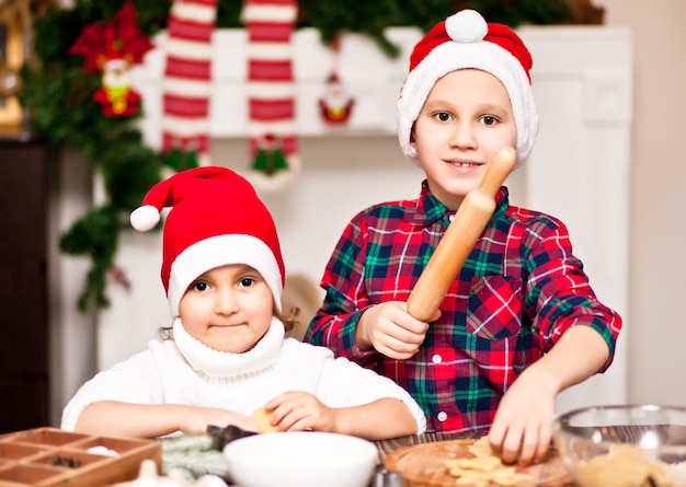 Kinder in einer Weihnachtsmütze backen Weihnachtsplätzchen zu Hause