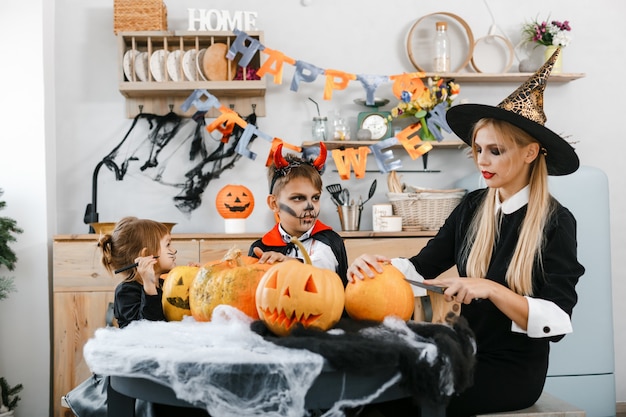 Kinder in Halloween-Kostümen schnitzen gruselige Augen und Münder auf Kürbisse. Hochwertiges Foto