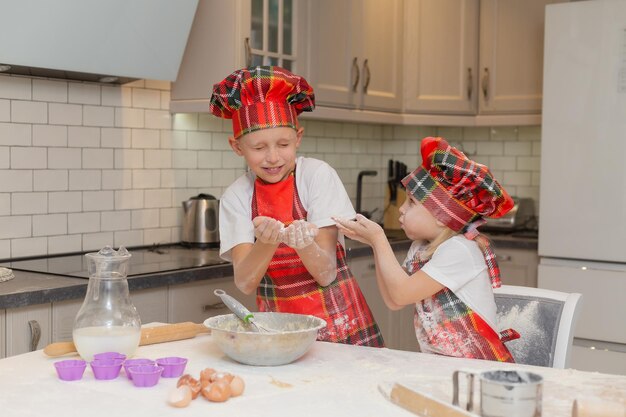 Kinder in Kochkostümen bereiten Teig aus Mehl, Milch, Eiern für Weihnachtsgebäck zu. bruder und schwester kochen festliches abendessen, kekse für neujahr in der küche. Winterkonzept des neuen Jahres