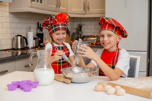 Kinder in Kochkostümen bereiten Teig aus Mehl, Milch, Eiern und Butter für Weihnachtsgebäck zu