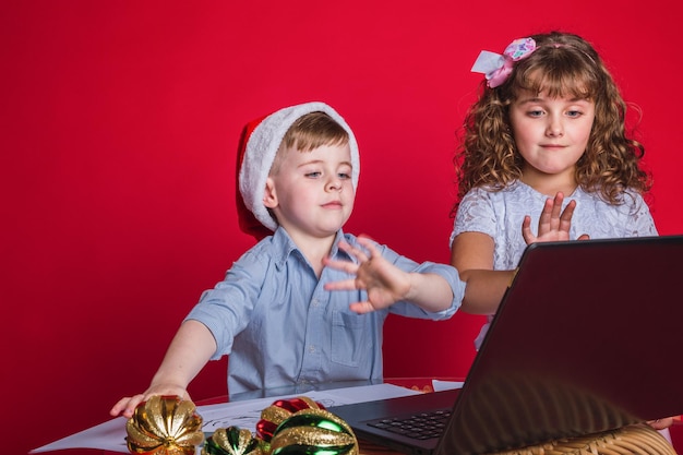 Foto kinder in weihnachtsmützen winken mit einem laptop. weihnachtskonzept.