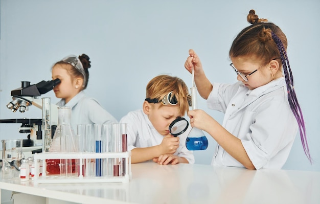 Kinder in weißen Mänteln spielen einen Wissenschaftler im Labor, indem sie Geräte verwenden