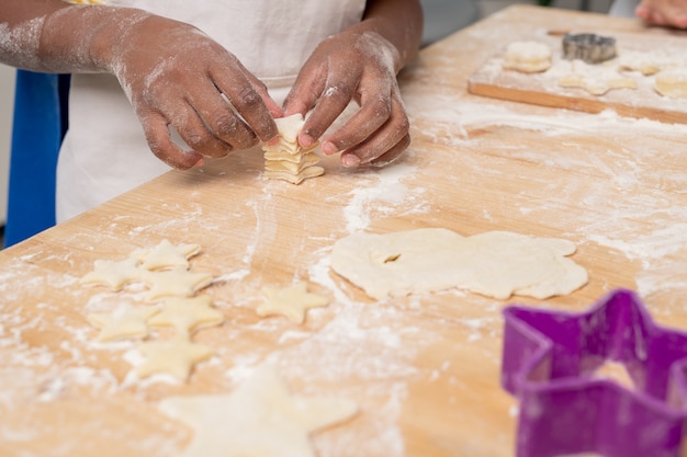 Kinder in weißen Schürzen schneiden Figuren in ausgerolltem Teig und backen leckere Kekse für den Urlaub