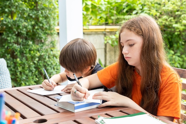 Kinder Junge und Mädchen machen Hausaufgaben und zeichnen zusammen im Garten zu Hause