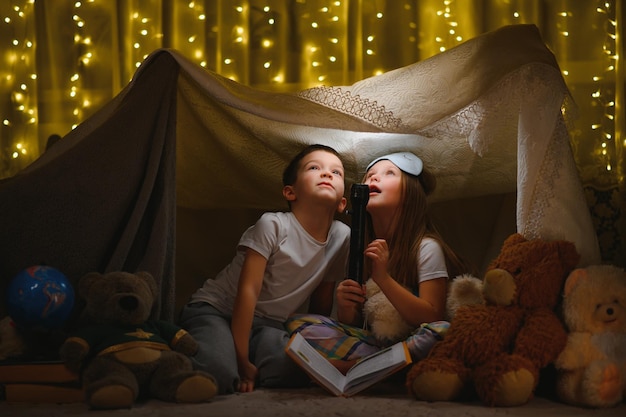 Kinder Junge und Mädchen spielen und erschrecken sich nachts mit Taschenlampe im Zelt