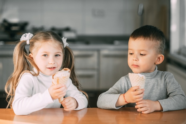 Kinder Jungen und Mädchen essen Eistüte in der Küche ist eine Menge Spaß sehr süß