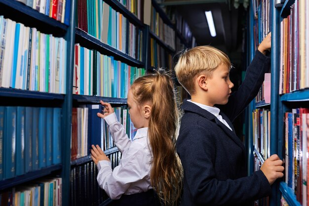 Kinder Jungen und Mädchen wählen Bücher in der Bibliothek für die Schule, gehen lesen, lernen