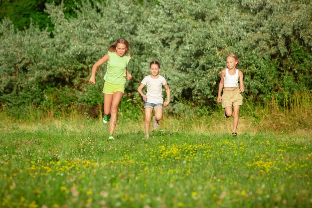 Kinder, Kinder, die im Sommersonnenlicht auf der Wiese laufen