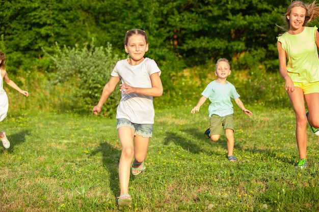 Kinder, Kinder, die im Sommersonnenlicht auf der Wiese laufen