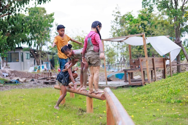 Kinder klettern auf Holzgeländer Vielfältige glückliche Kindergruppe, die auf dem Spielplatz beim Lernen im Sommercamp spielt