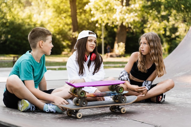 Kinder lächeln und lachen und haben gemeinsam Spaß Kinder mit Skateboard und Penny Boards kommunizieren und diskutieren auf dem Sportplatz Freundschaftskonzept für Jungen und Mädchen