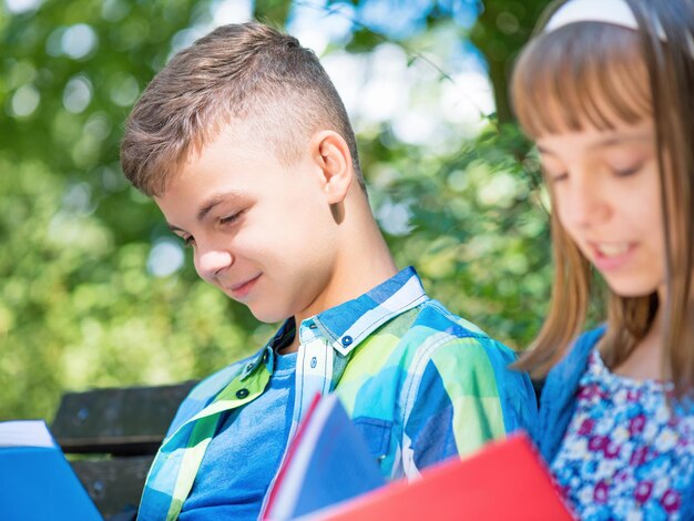 Kinder lesen Bücher im Park Außenporträt von Teenager-Jungen und -Mädchen Geschwister machen Hausaufgaben im Sommergarten Schöne Kinder lernen im Schulhof