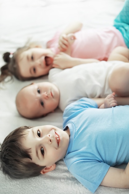 Kinder liegen auf dem Bett neben dem Neugeborenen, kleine Schwester. Emotionen der Kinder.