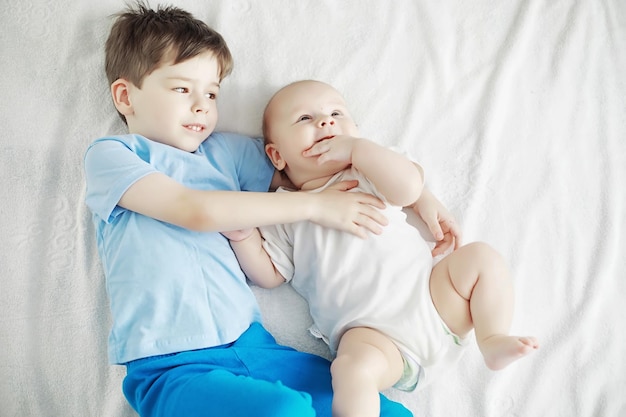 Kinder liegen auf dem Bett neben dem Neugeborenen, kleine Schwester. Emotionen der Kinder.