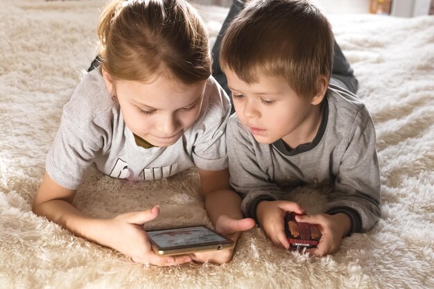 Foto kinder liegen auf dem bett und schauen sich zeichentrickfilme an, die ein spiel auf dem smartphone spielen