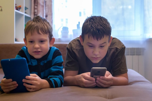 Kinder liegen auf der Couch und spielen in Smartphones