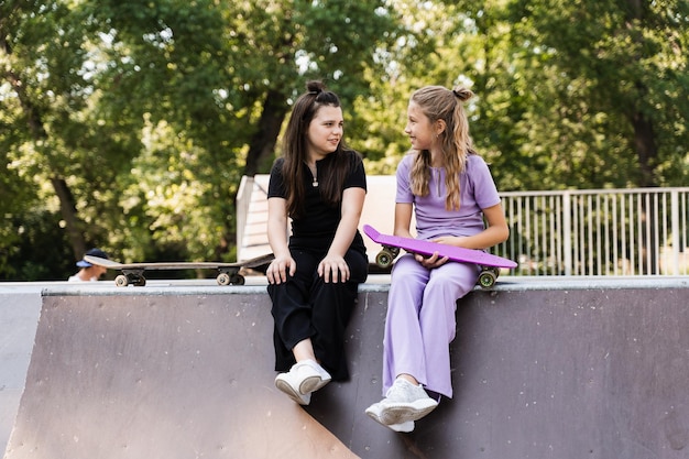 Kinder Mädchen lächeln und lachen und haben gemeinsam Spaß Kinder mit Skateboard und Penny Boards kommunizieren und diskutieren auf dem Sportplatz Mädchenfreundschaftskonzept