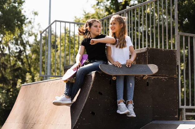 Kinder Mädchen lächeln und lachen und haben gemeinsam Spaß Kinder mit Skateboard und Penny Boards kommunizieren und diskutieren auf dem Sportplatz Mädchenfreundschaftskonzept